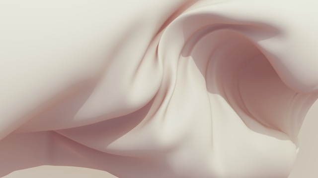 Soft flowing fabric in cream and pale pink tones with gentle curves and folds creating an ethereal, organic skin texture.